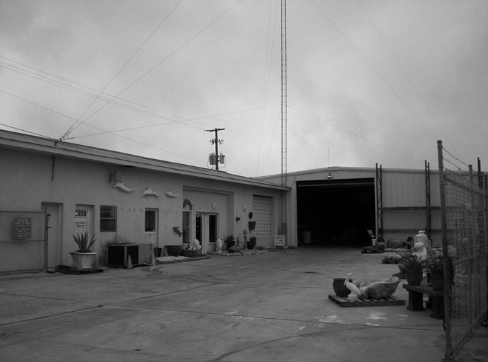 Warehouse with open garage door and art objects on pavement outside.